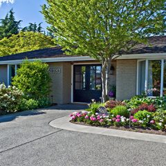 This is a pretty house a ramble on the exterior front doorway area. Lots of landscaping plants and trees and large windows make this a very welcoming home.