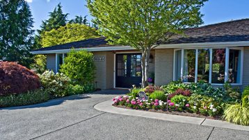 This is a pretty house a ramble on the exterior front doorway area. Lots of landscaping plants and trees and large windows make this a very welcoming home.